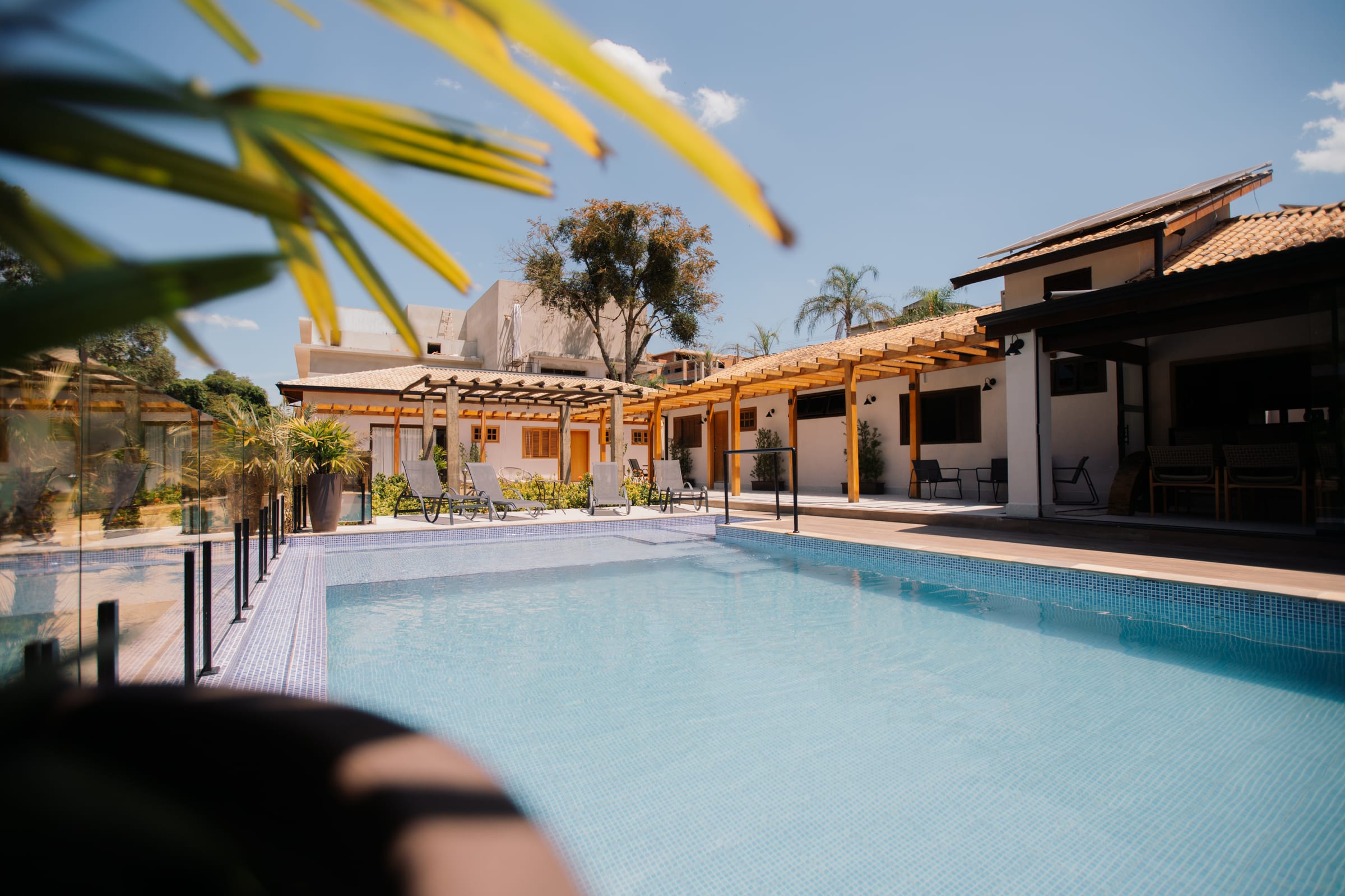 Piscina da Morada do Vale com espreguiçadeiras e, ao fundo, os chalés de telhado de barro e pérgola de madeira.