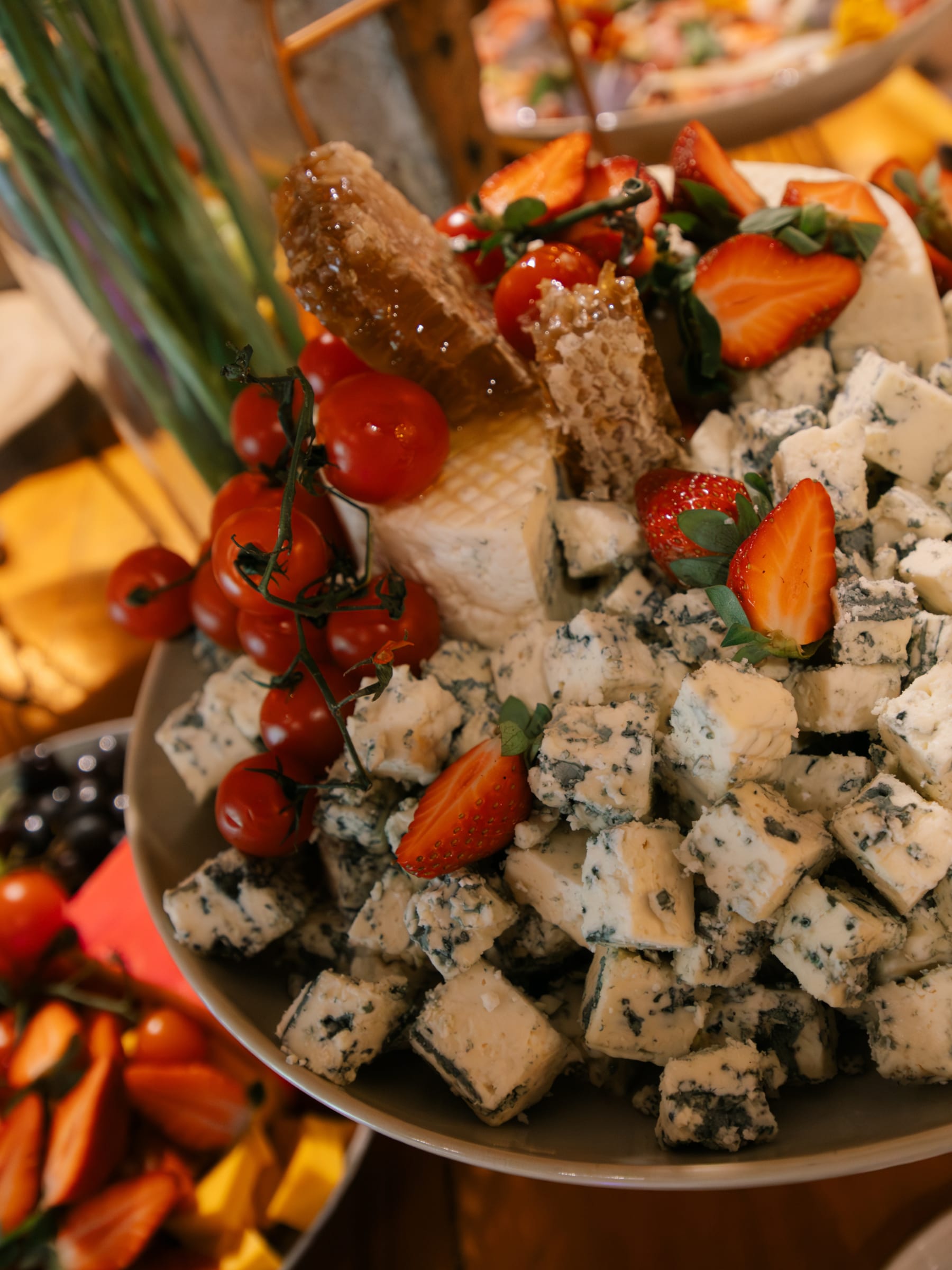 Travessa de queijo gorgonzola em cubos com favo de mel, morangos e tomates-cereja no ramo.