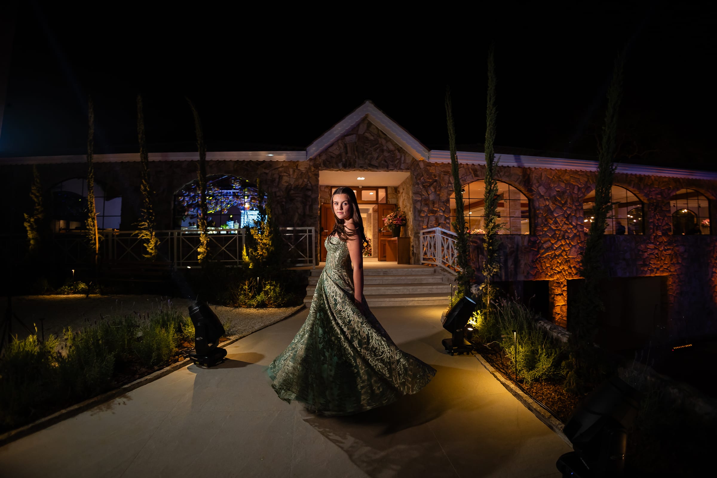 Debutante de vestido verde girando no caminho iluminado, à noite.